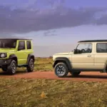 Zwei Suzuki Jimny-Modelle, ein Dreitürer in Grün und ein Fünftürer XL in Beige, auf einer Piste im Gelände