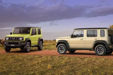 Zwei Suzuki Jimny-Modelle, ein Dreitürer in Grün und ein Fünftürer XL in Beige, auf einer Piste im Gelände