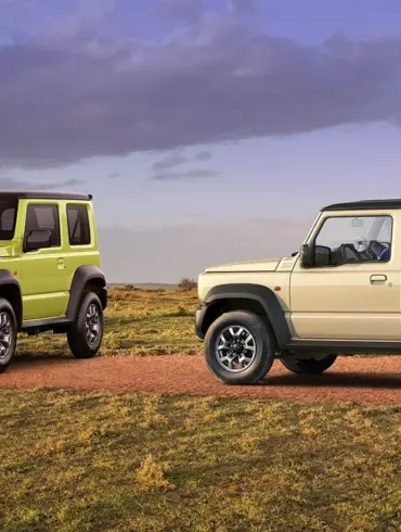 Zwei Suzuki Jimny-Modelle, ein Dreitürer in Grün und ein Fünftürer XL in Beige, auf einer Piste im Gelände