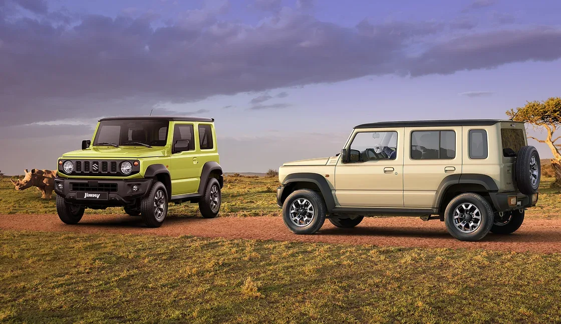 Zwei Suzuki Jimny-Modelle, ein Dreitürer in Grün und ein Fünftürer XL in Beige, auf einer Piste im Gelände