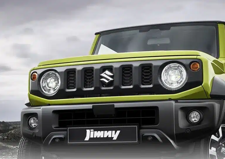 Frontansicht eines Suzuki Jimny in grün mit schwarzem Kühlergrill und runden Scheinwerfern.