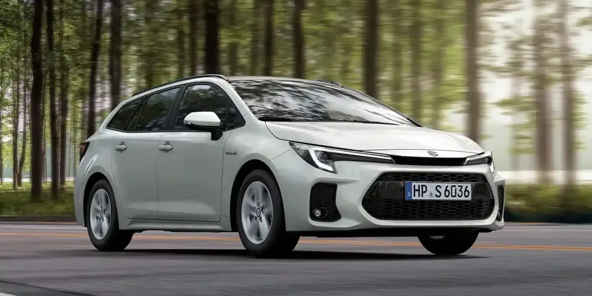 Weißer Suzuki Swace Hybrid fährt auf einer Straße durch einen Wald, Seitenansicht, Tageslicht.