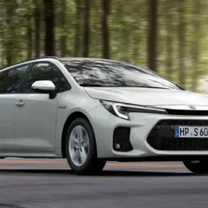 Weißer Suzuki Swace Hybrid fährt auf einer Straße durch einen Wald, Seitenansicht, Tageslicht.