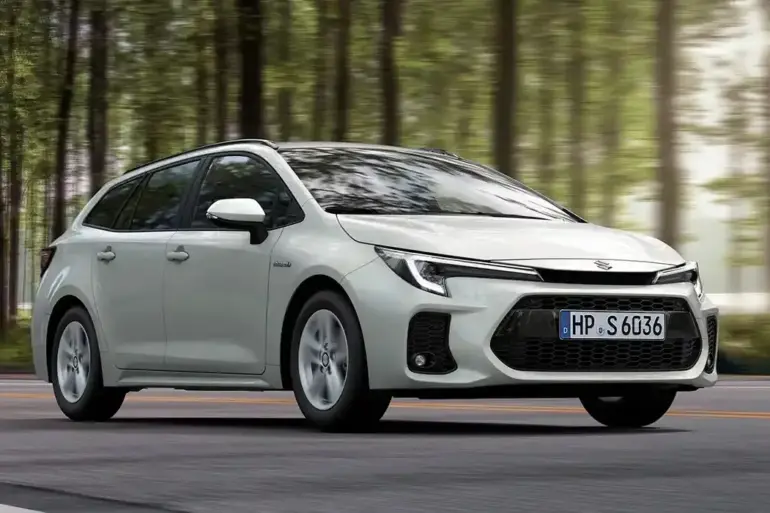 Weißer Suzuki Swace Hybrid fährt auf einer Straße durch einen Wald, Seitenansicht, Tageslicht.
