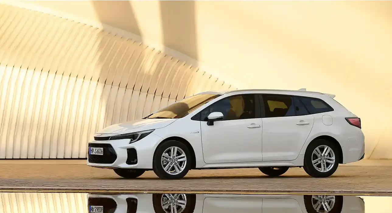Weißer Suzuki Swace Kombi vor moderner Architektur, Seitenansicht, ruhige Atmosphäre.
