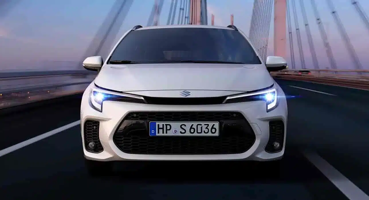 Frontaufnahme eines weißen Suzuki Swace, der auf einer Brücke fährt. Deutlich erkennbar sind der große hexagonale Kühlergrill und die LED-Scheinwerfer.