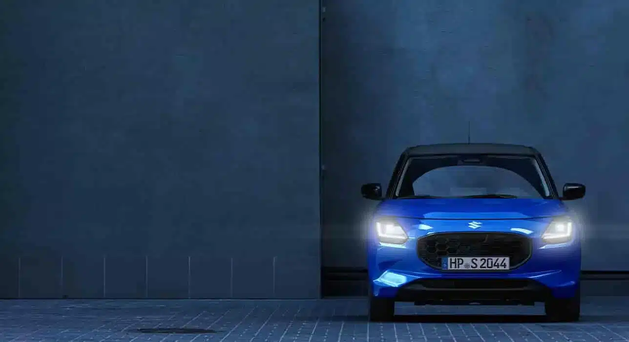 Suzuki Swift 2024 in Blau von vorne, Scheinwerfer eingeschaltet, moderne Kleinwagen-Optik