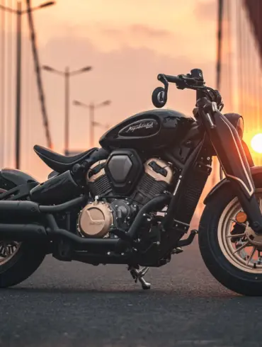 Napoleonbob 500 Motorrad, seitliche Ansicht, stilvoll inszeniert bei Sonnenuntergang auf einer modernen Brücke.
