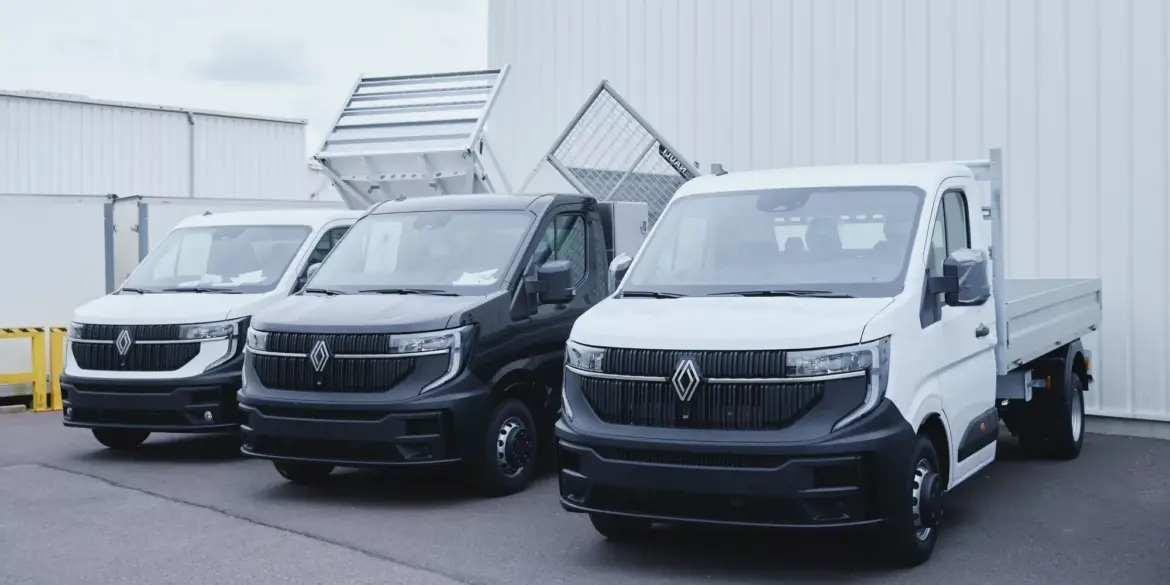 Drei werksseitig umgebaute Renault Nutzfahrzeuge, darunter ein Dreiseitenkipper, vor einem Fabrikgebäude