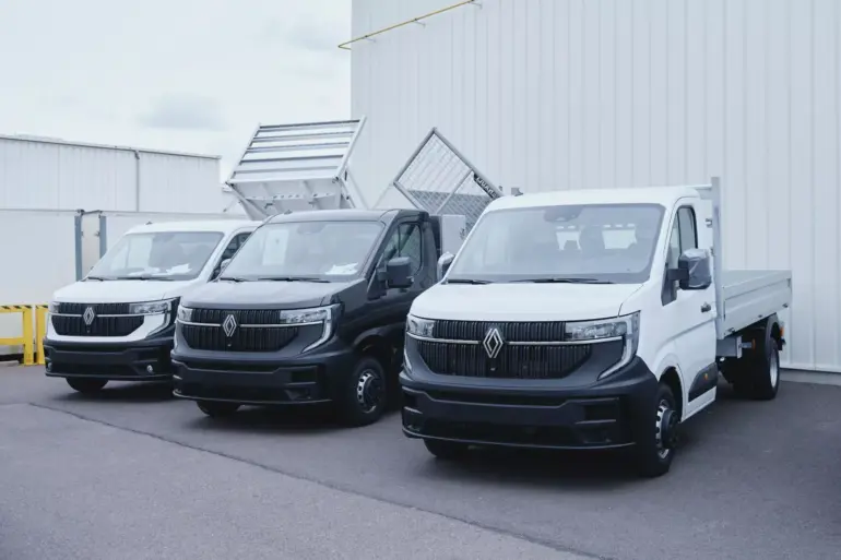 Drei werksseitig umgebaute Renault Nutzfahrzeuge, darunter ein Dreiseitenkipper, vor einem Fabrikgebäude