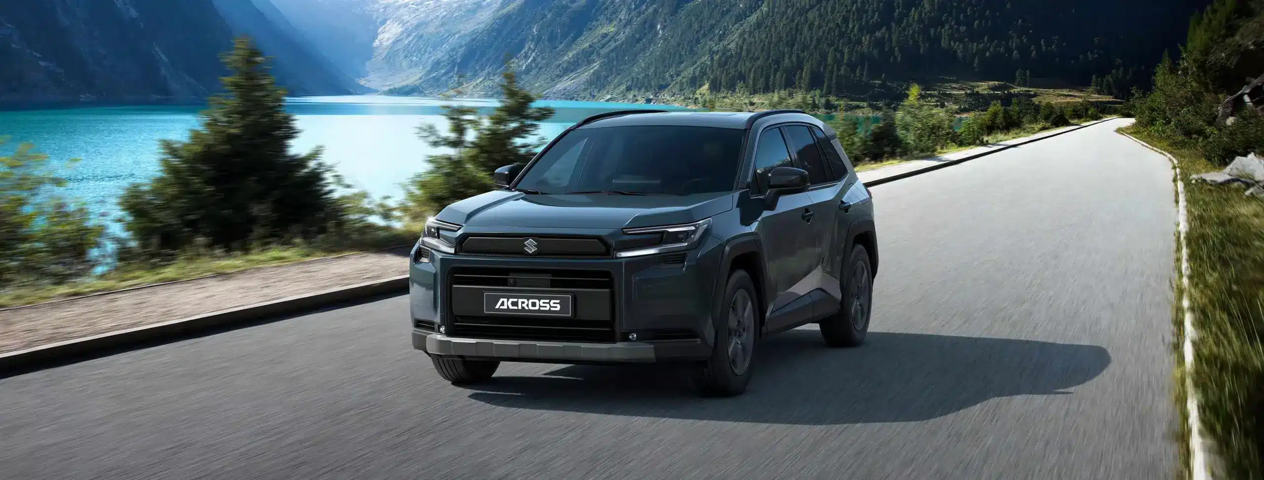 Suzuki Across Plug-in-Hybrid SUV fährt auf einer Landstraße entlang eines Sees in einer Berglandschaft