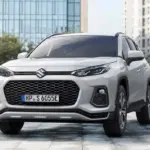 Suzuki Across Plug-in-Hybrid SUV aus der Frontperspektive, Weiß, steht auf einem Platz vor modernen Gebäuden.