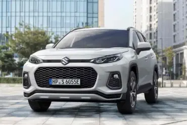 Suzuki Across Plug-in-Hybrid SUV aus der Frontperspektive, Weiß, steht auf einem Platz vor modernen Gebäuden.
