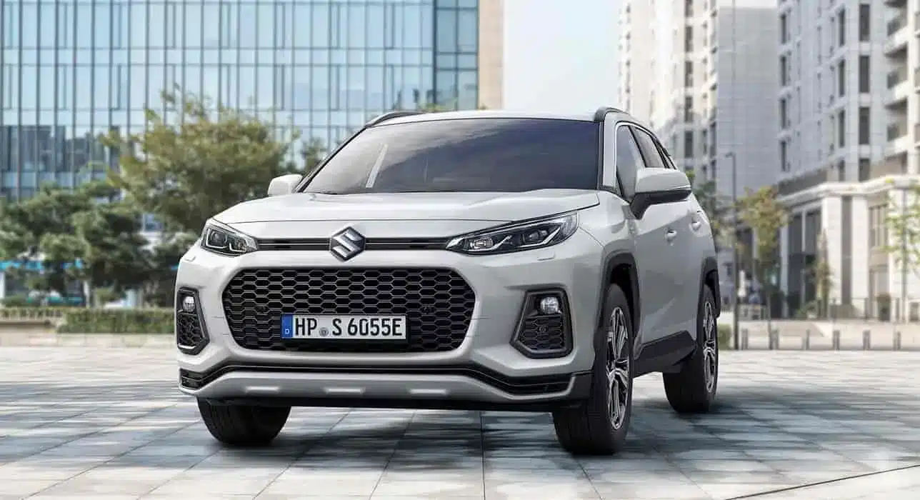 Suzuki Across Plug-in-Hybrid SUV aus der Frontperspektive, Weiß, steht auf einem Platz vor modernen Gebäuden.