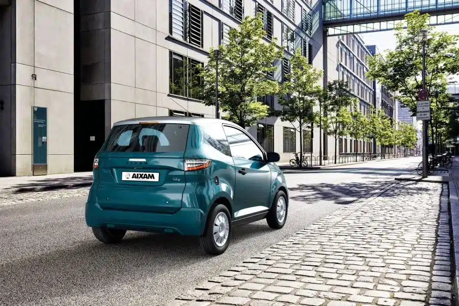 Aixam E City Pack elektrisches Leichtfahrzeug in einer modernen Stadtstraße, Rückansicht, türkisfarbene Lackierung.