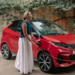 Roter Aixam E Coupé GTi wird von einer Frau an der Ladestation angeschlossen.