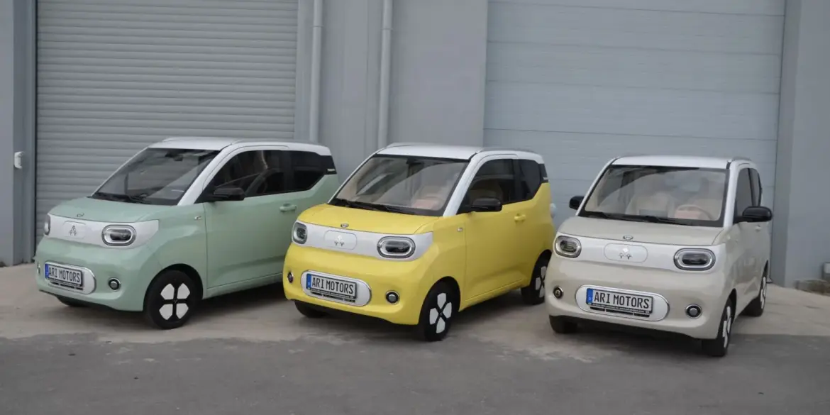 Drei ARI Bruni Elektroautos nebeneinander, pastellgrün, gelb und weiß, vor Garagentoren