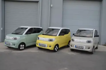Drei ARI Bruni Elektroautos nebeneinander, pastellgrün, gelb und weiß, vor Garagentoren