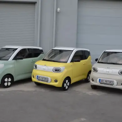 Drei ARI Bruni Elektroautos nebeneinander, pastellgrün, gelb und weiß, vor Garagentoren