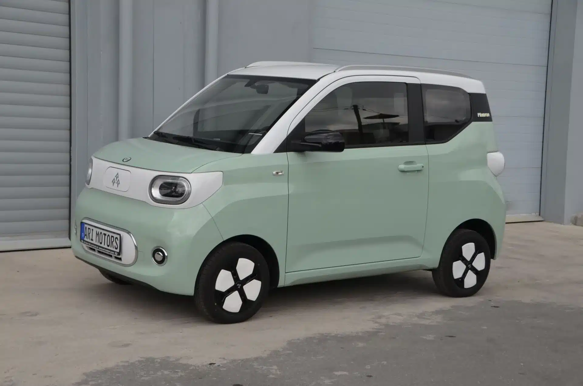 ARI Bruni 2-Sitzer Elektroauto in mintgrün-weiß, stehend vor grauer Industriehalle