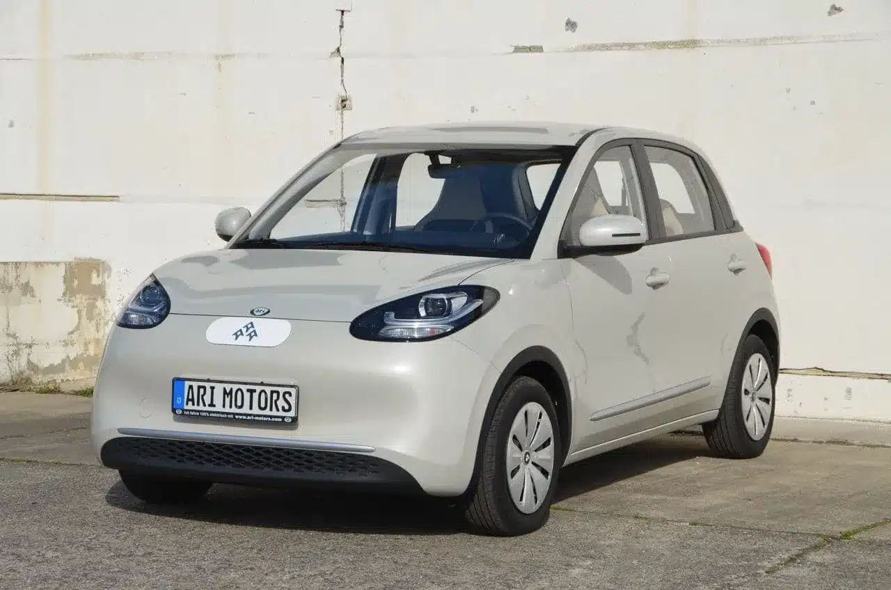 Front- und Seitenansicht eines weißen ARI Poly Elektroautos von ARI Motors im urbanen Umfeld.