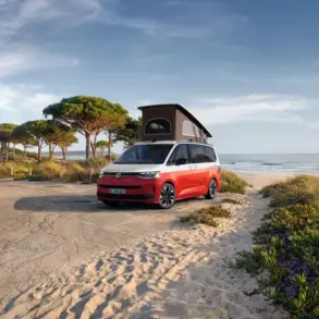 VW California Ocean „Generation“ in Candy-Weiß/Sunset Red Metallic mit Aufstelldach am Strand geparkt