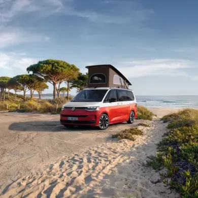 VW California Ocean „Generation“ in Candy-Weiß/Sunset Red Metallic mit Aufstelldach am Strand geparkt