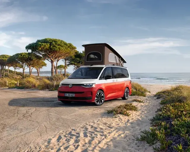 VW California Ocean „Generation“ in Candy-Weiß/Sunset Red Metallic mit Aufstelldach am Strand geparkt