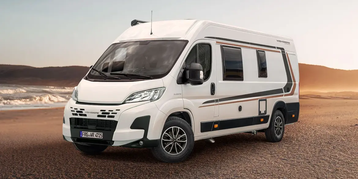 WEINSBERG CaraBus EDITION [FIRE] Camper Van steht auf sandigem Untergrund vor einer Meereskulisse.