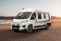 WEINSBERG CaraBus EDITION [FIRE] Camper Van steht auf sandigem Untergrund vor einer Meereskulisse.