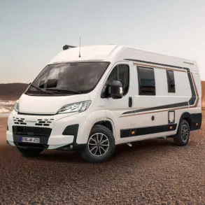 WEINSBERG CaraBus EDITION [FIRE] Camper Van steht auf sandigem Untergrund vor einer Meereskulisse.