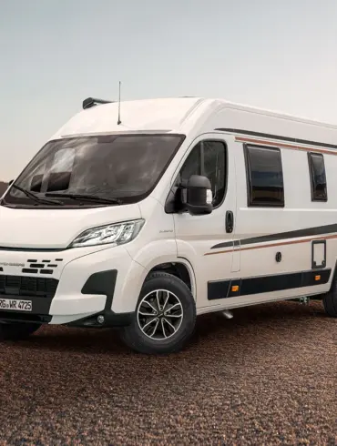 WEINSBERG CaraBus EDITION [FIRE] Camper Van steht auf sandigem Untergrund vor einer Meereskulisse.