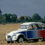 Citroën 2CV Cocorico Sonderedition in Blau, Weiß und Rot auf einem Stoppelfeld, seitliche Ansicht, ländliche Kulisse.