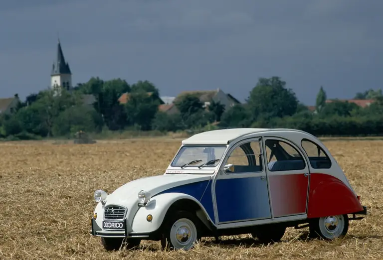 Citroën 2CV Cocorico Sonderedition in Blau, Weiß und Rot auf einem Stoppelfeld, seitliche Ansicht, ländliche Kulisse.