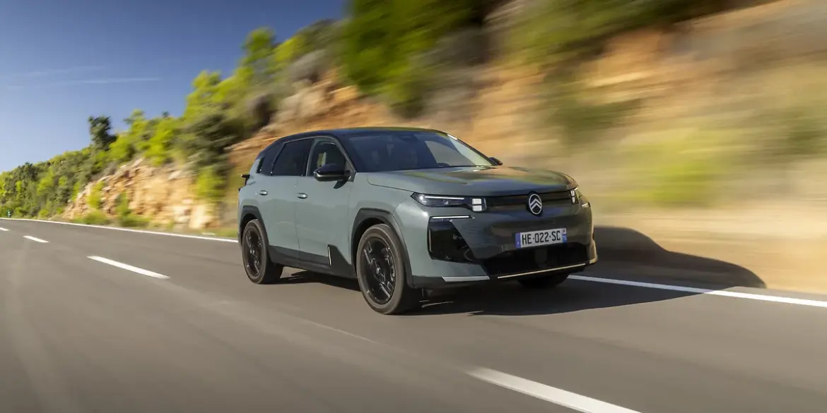 Citroën C5 Aircross 230 Long Range in heller Lackierung fährt dynamisch auf einer Landstraße vor Felswand und Bäumen