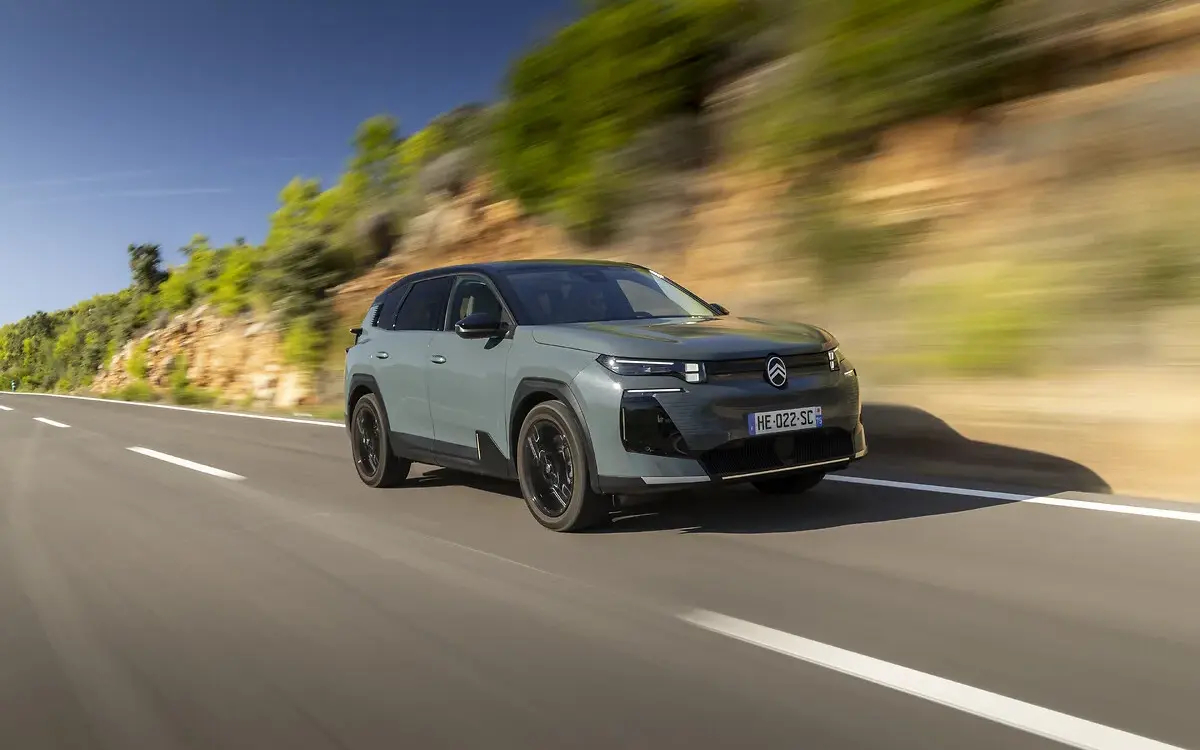 Citroën C5 Aircross 230 Long Range in heller Lackierung fährt dynamisch auf einer Landstraße vor Felswand und Bäumen