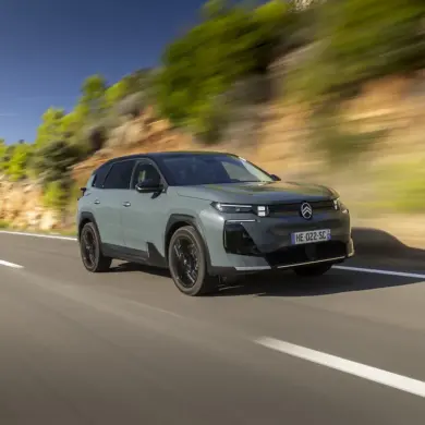 Citroën C5 Aircross 230 Long Range in heller Lackierung fährt dynamisch auf einer Landstraße vor Felswand und Bäumen