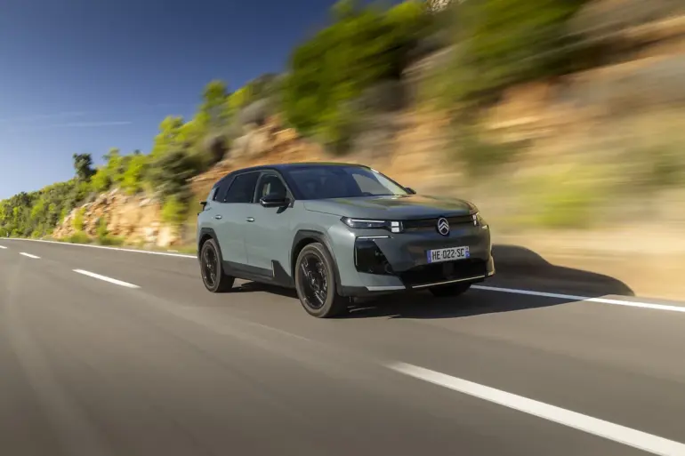 Citroën C5 Aircross 230 Long Range in heller Lackierung fährt dynamisch auf einer Landstraße vor Felswand und Bäumen