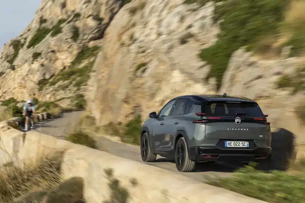 Heckansicht des Citroën C5 Aircross 230 Long Range beim Fahren auf einer Landstraße mit Felsen im Hintergrund
