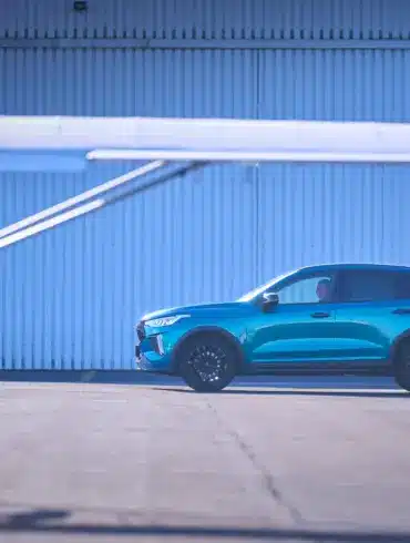 Seitliche Ansicht des GWM HAVAL Jolion Pro in Blau, geparkt auf einem Flugplatz mit Flugzeug im Vordergrund.