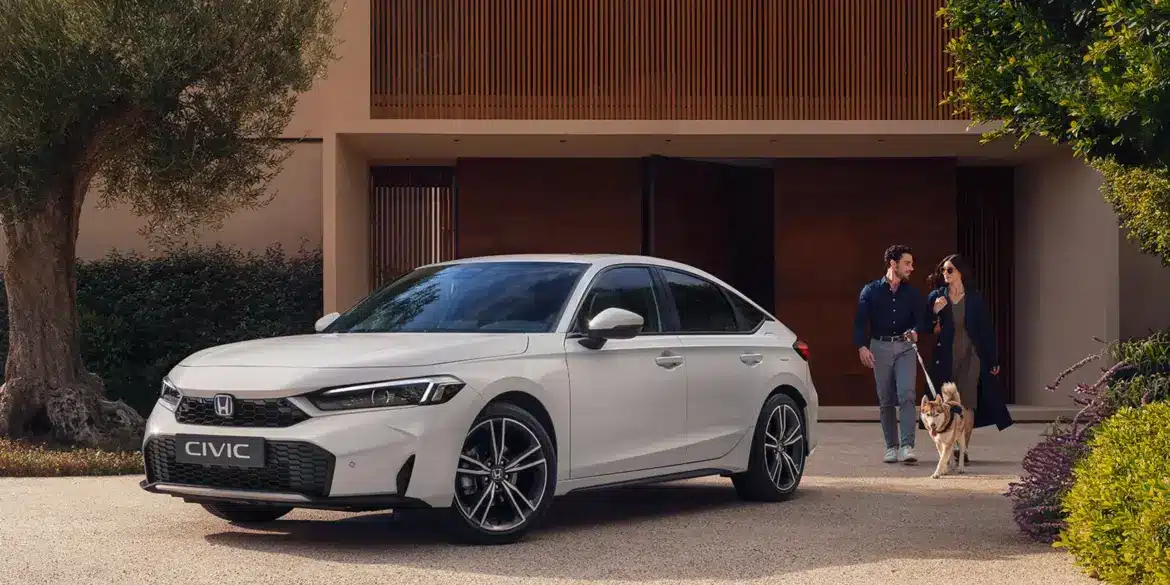 Weißer Honda Civic e:HEV steht vor einem modernen Haus, im Vordergrund ein Paar mit Hund.