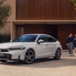 Weißer Honda Civic e:HEV steht vor einem modernen Haus, im Vordergrund ein Paar mit Hund.