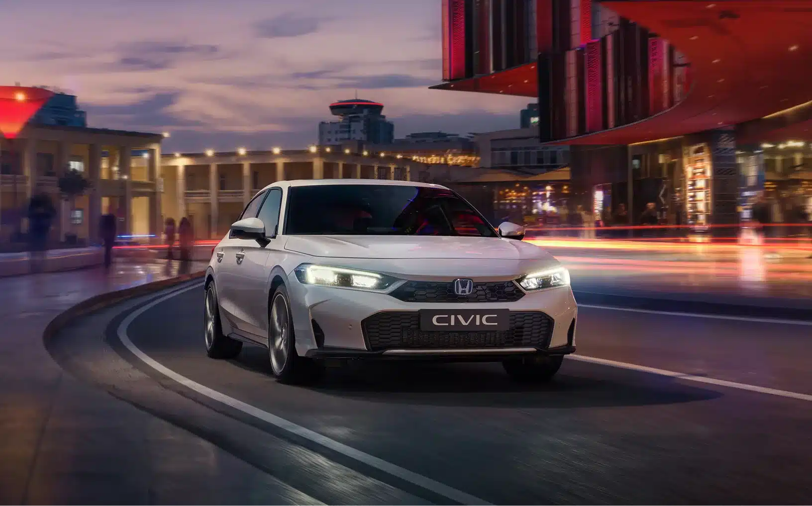 Honda Civic e:HEV, Frontansicht, fahrend in urbaner Umgebung am Abend.