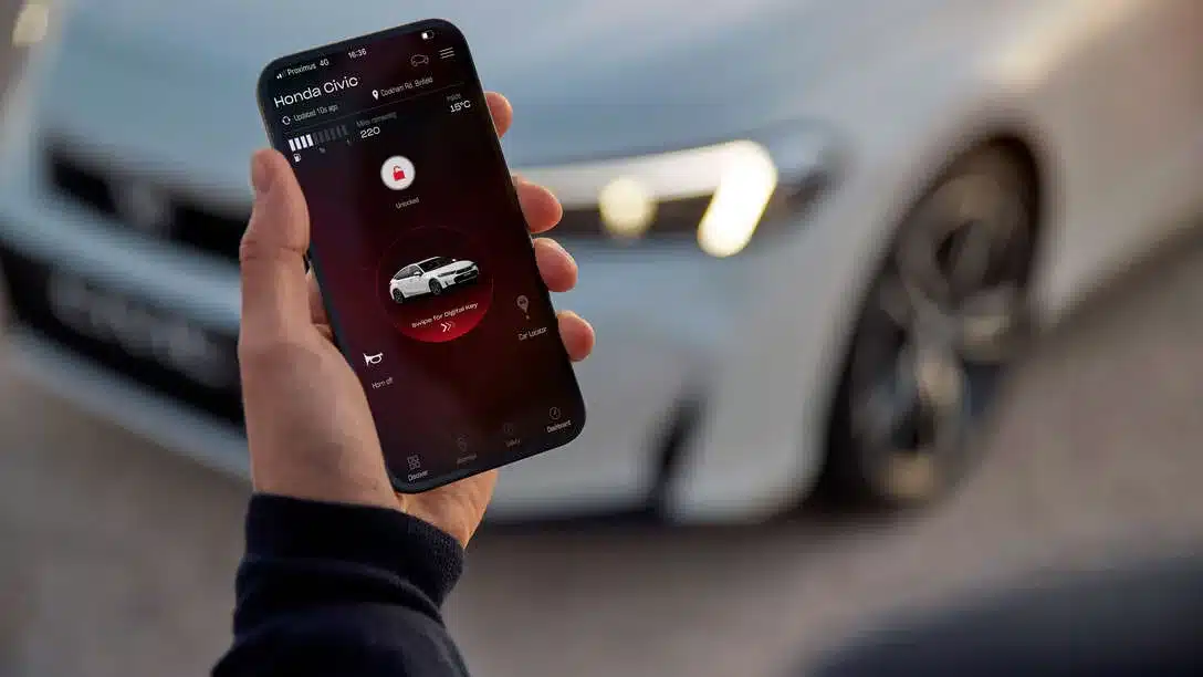 Hand hält Smartphone mit geöffneter My Honda+ App vor weißem Honda Civic e:HEV