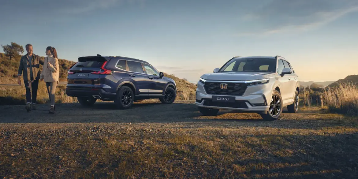 Zwei Honda CR-V der aktuellen Generation, einer von vorne und einer von hinten, auf einem Feldweg bei Sonnenuntergang.