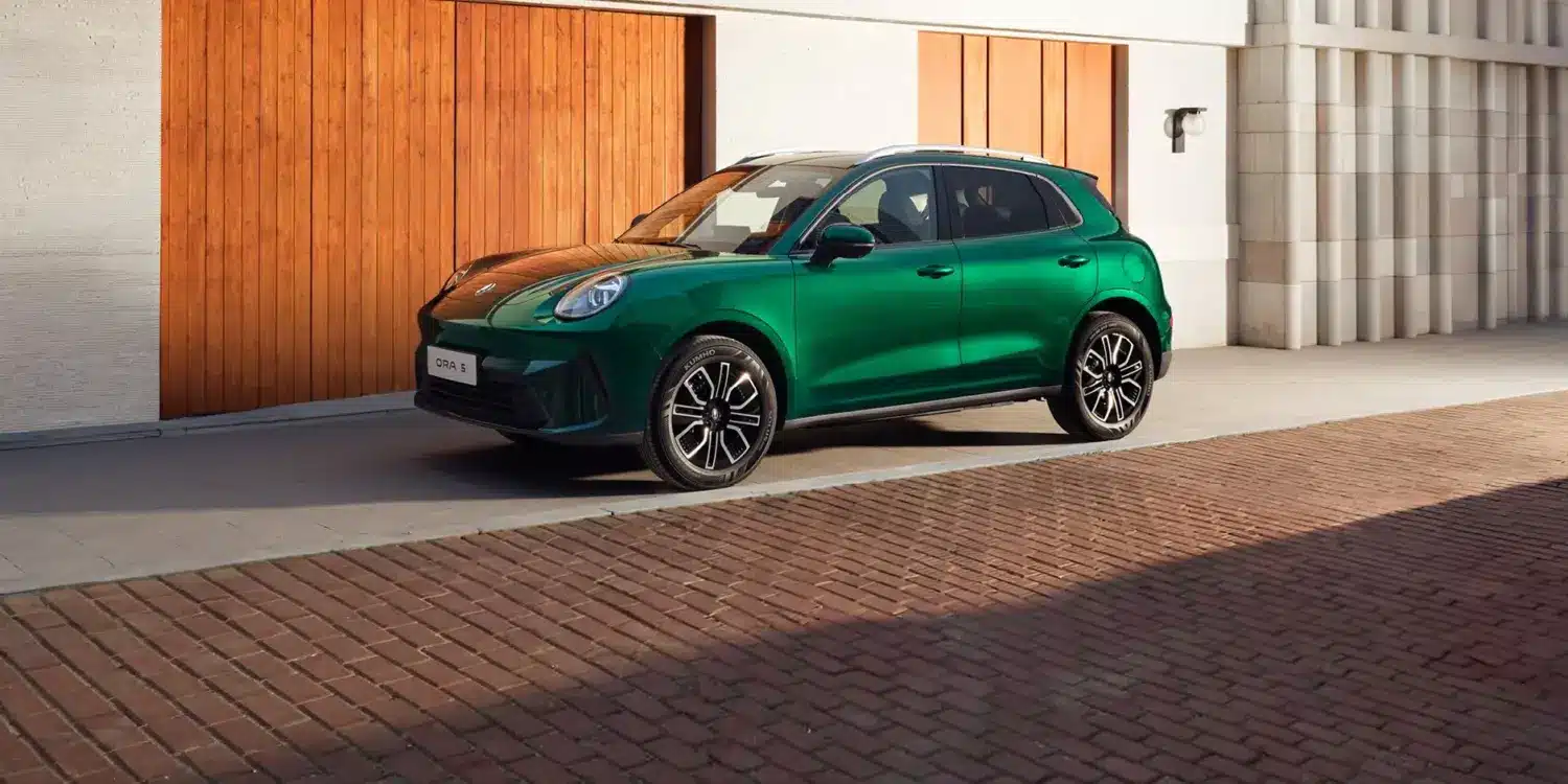 Grüner GWM ORA 5 SUV seitlich vor einer Holzfassade geparkt