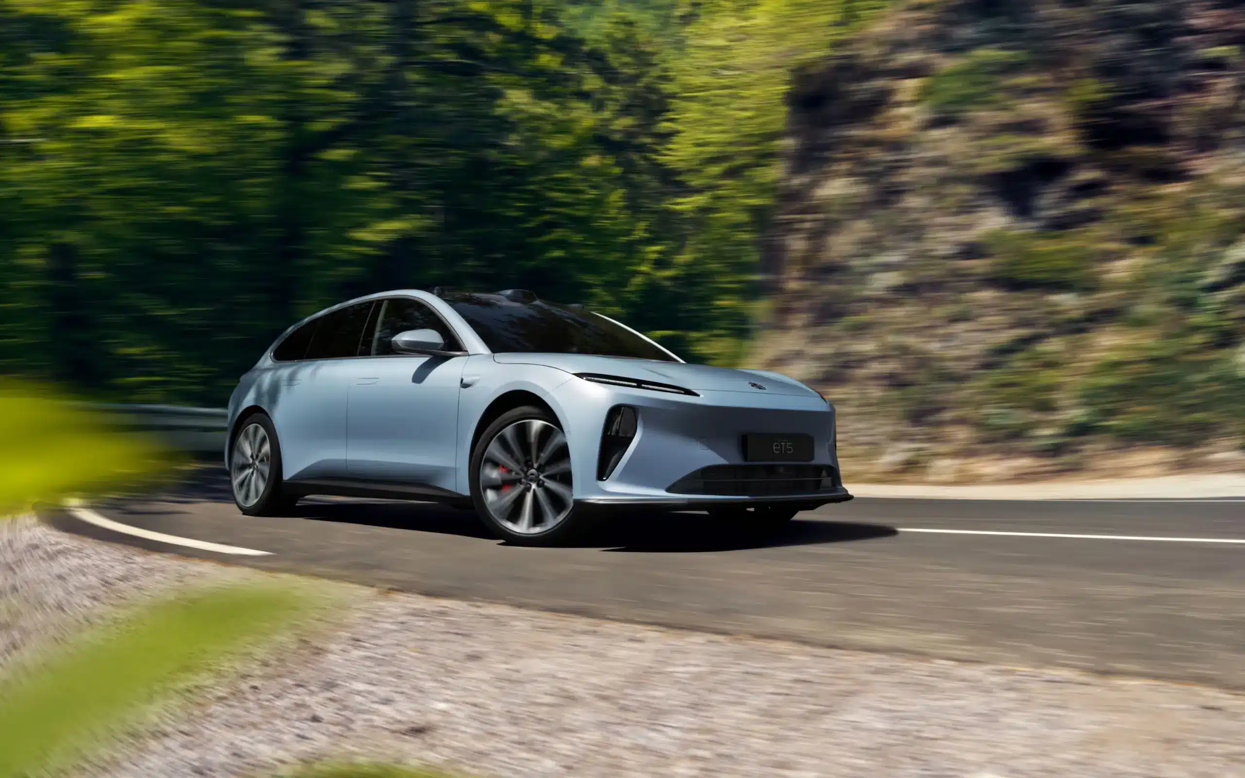 NIO ET5 Touring fährt dynamisch durch eine grüne Landschaft auf kurviger Straße.