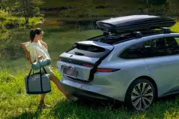 Eine Frau öffnet freihändig den Kofferraum eines silbernen NIO ET5 Touring, der mit Dachbox am Ufer eines Sees steht.
