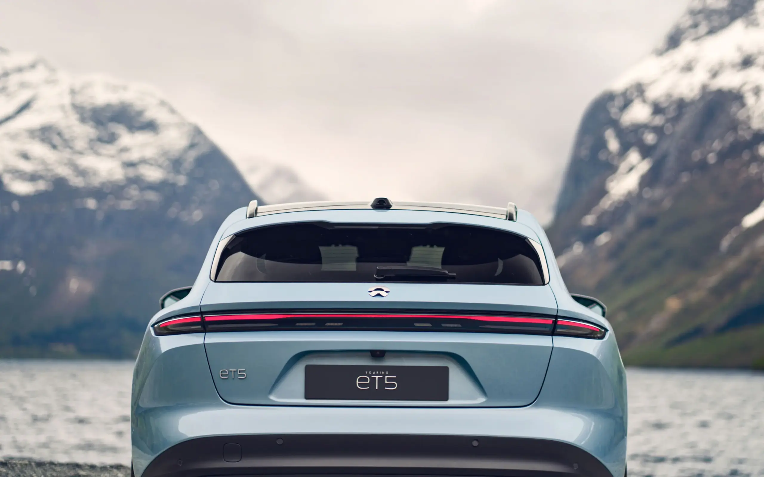 Heck des NIO ET5 Touring in blauer Lackierung, im Vordergrund Wasser, im Hintergrund schneebedeckte Berge.