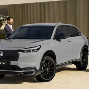 Honda HR-V e:HEV in Grau mit schwarzem Grill, geparkt vor moderner Architektur, zwei Personen daneben.